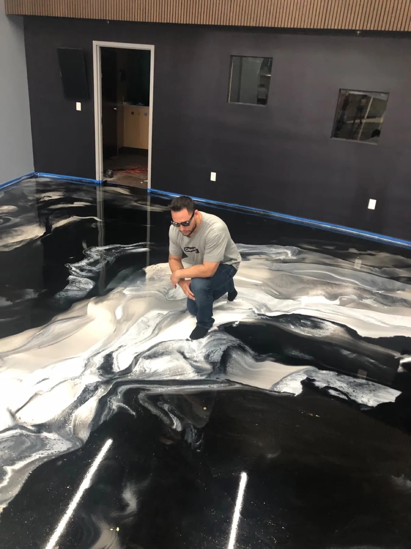 Owner crouched on a black and white marbled metallic epoxy floor in a dark-walled room in Wayne County, North Carolina