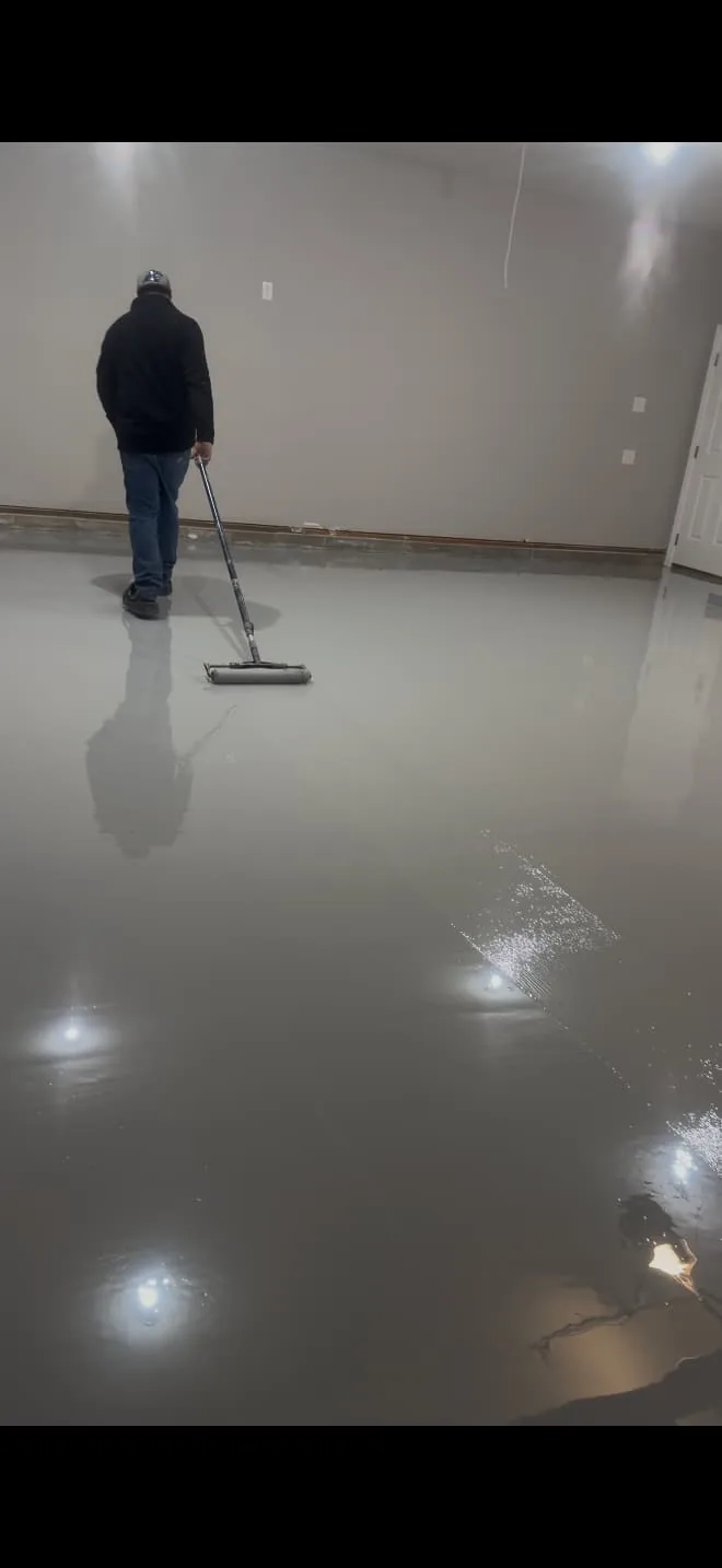 Owner rolling a gray coat across an interior floor with a long-handled roller in Wayne County, North Carolina