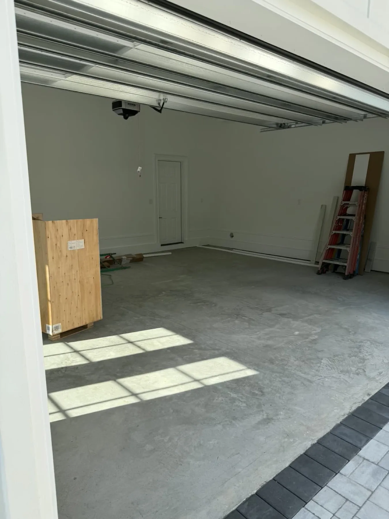 Bare garage slab with window light across it and a plywood crate and red ladder along the wall in Wayne County, North Carolina